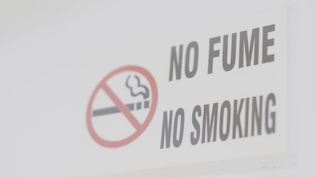 A bilingual sign of no smoking is displayed on a white wall of a room. The red symbol is seen crossing out a cigarette.
