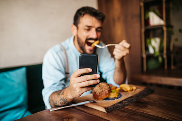Fototapeta na wymiar Handsome middle age man sitting in restaurant and enjoying in delicious burger. He is happy and smiled and uses his smart phone to talk with someone.