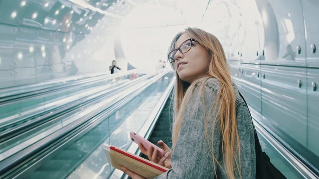 Young working girl fascinated by the modern Warsaw metro, standing on the escalator