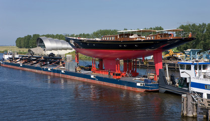 Transport of a super sailing yacht on a pontoon on the river.  Keteldiep. Netherlands. Tugboat. Zwarte meer. keteldiep. Ramspol.  Balgstuw. Bellows weir.