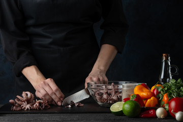 Chef cuts seafood, octopus for cooking, on the background of vegetables, oriental cuisine, asian food.Thai cuisine, cookery and recipe book