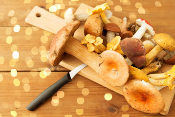 cooking, culinary and edible mushrooms concept - different edible mushrooms and kitchen knife on wooden cutting board