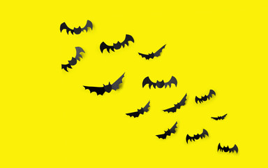 halloween, decoration and scary concept - flock of black paper bats flying over yellow background