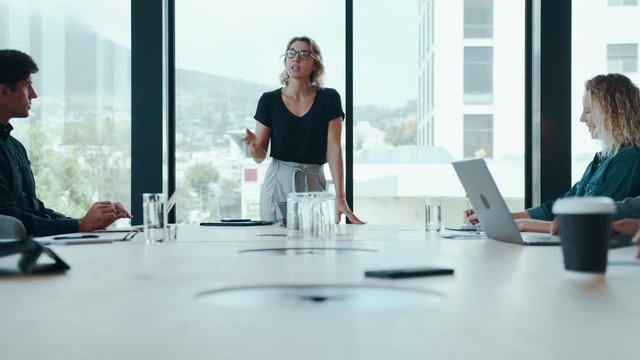Female entrepreneur explaining new strategies to colleagues in meeting room. Businesswoman discussing work with team in boardroom.
