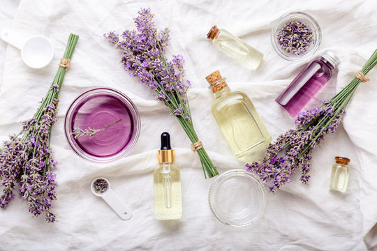 Lavender oils serum and lavender flowers on white fabric. Skincare cosmetics products. Set natural spa beauty products. Lavender essential oil, serum, body butter, massage oil, liquid. Flat lay