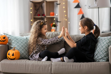 halloween, holiday and childhood concept - smiling little girls in costumes playing clapping game at home