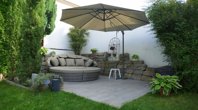 Gartenterrasse mit Loungegruppe und Sonnenschirm in einer Gartenecke mit Säulen-Faulbaum und umgeben von Pflanzen und Zypressen	