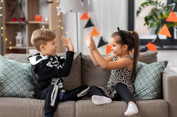 halloween, holiday and childhood concept - smiling little boy and girl in costumes playing clapping...