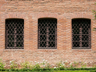 Outside wall of a medieval old building with three windows and bars. Brancovenesc or Romanian Renaissance architectural style.