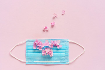 Ein blauer Mundschutz mit kleinen rosa Blüten auf einen pinken Hintergrund. Flat lay, Hygiene,...