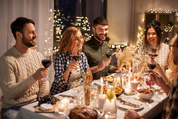 holidays, celebration and people concept - happy friends having christmas dinner at home drinking non-alcoholic red wine