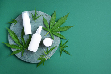 Hemp cosmetic products white bottles with oil, hemp seed extract, cream and cannabis leaves on green background. Flat lay. Top view. Copy space. Natural skin care and body treatment
