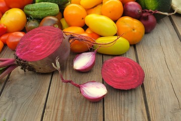 Sliced ​​beets and onions lie on a wooden board against a background of different bright vegetables. Harvest and cooking concept.