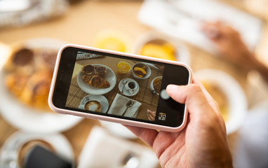 Top view close up of young female hands taking picture of perfectly served breakfast on her smartphone in a luxury hotel during holidays vacation.