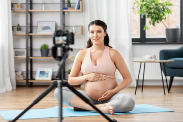 Fototapeta na wymiar sport, blogging and people concept - happy pregnant woman or blogger with camera on tripod recording online yoga class at home