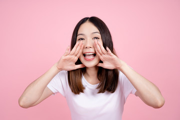 Beautiful Asian woman shouting and looking up, using her mouth to tell something or call someone on a pink background.