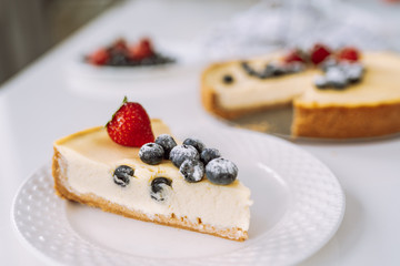 Piece of homemade cheesecake with fresh strawberry and blackberry on a white plate on a table.