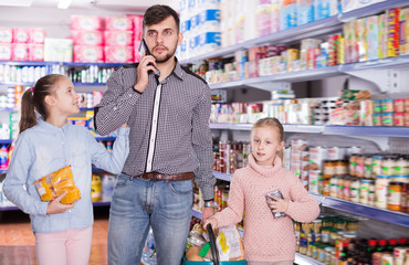 Adult father speaking phone while doing shopping with daughters in supermarket