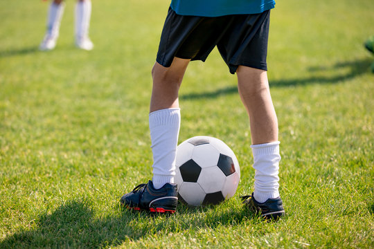 Football players feet close up. Sports training  on a grass field background. Boy in a sportswear. Player wearing white football socks and soccer cleats. Football horizontal background. Sport training
