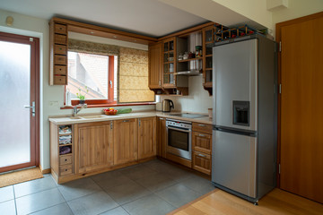 Corner kitchen with window in small apartment. Wooden furniture in warm tones, wide angle view..