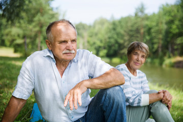 Happy Elderly Senior couple sitting on grass together relaxing on the shore of the lake. copy space