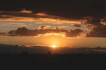 A rainy clouds at the sunset above city buildings silhouette background.