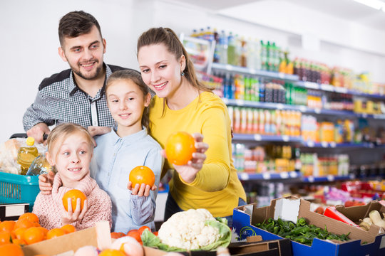 Nice parents with two daughters choosing sweet citrus fruits in food store