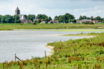 Zwolle, The Netherlands, July 21, 2020: river channel and wildflowers in the floodplains of the IJssel river with the church and houses of the village of Zalk on the other side.