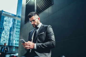 Calm pensive businessman interacting with smartphone in city