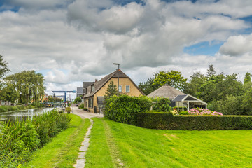 Fototapeta premium Village view towards Grote Brug, a drawbridge in Langeraar, with old farm buildings against a sky with gray clouds