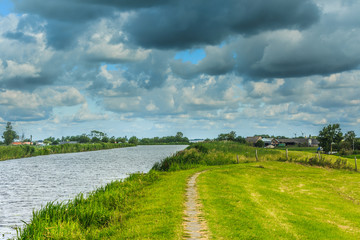 Landscape with bicycle footpath Smitskade between Leidse Vaart and Langeraarse plassen and the villages of Lageraar and Ter Aar with a green dike against a sky with gray-yellow clouds