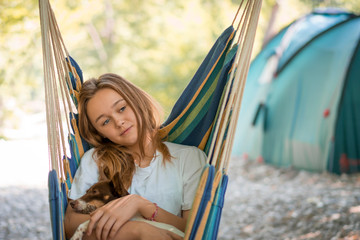 A young woman relaxing in a hammock with her dog. Girl resting in a hammock in the woods. Camping, healthy lifestyle in the forest.