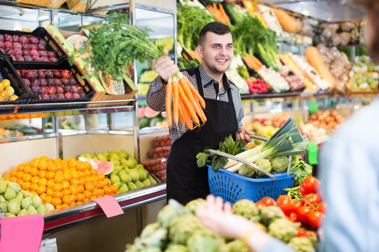 Happy man seller helping customer to buy fruit and vegetables in grocery shop