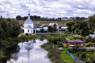 Rural summer cloudy landscape with river and white church