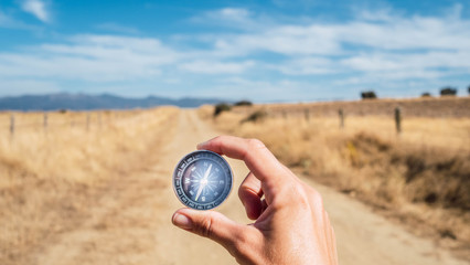 Detail of a hand with a compass on a dirt road with mountains on the horizon and blue sky. Concept: adventure, travel, self-knowledge