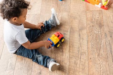 Overhead view of African American boy in jeans playing with toy truck on wooden floor - Powered by Adobe