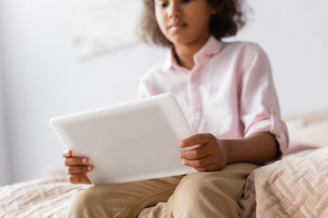 low angle view of african american girl in white shirt using digital tablet in bedroom