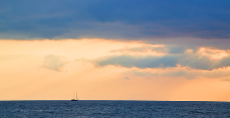 Ocean scenery. Sunset and Virgin nature landscape. Beautiful golden sky. Calming water. Floating boat on horizon.