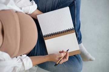 pregnant woman writes in a notebook with copy space
