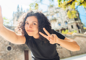 Young pretty woman taking a selfie, sends an air kiss, shows a V sign in front of an old castle, Sintra, Portugal