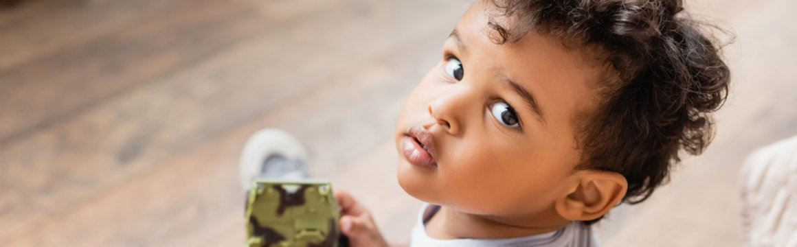 horizontal image of african american boy looking at camera while holding toy, overhead view