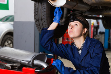 Female is standing near car and repairing it in workshop