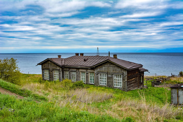 Fototapeta na wymiar abandoned wooden house on the background of lake Baikal and cloudy sky