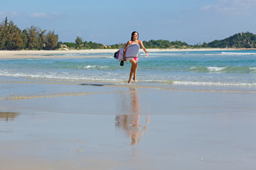 Fototapeta premium young slender and tanned girl in a swimsuit with a surfboard in her hands on the beach near the water, sea, summer, heat, sunny day, clear sea water, wave, lifestyle, sports, leisure, vacation, weeken