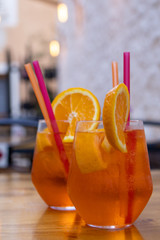 Two elegant glasses of Aperol-Spritz-Drinks  with pink and orange straws and decorative orange...