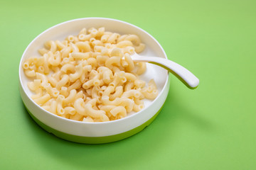 boiled pasta on child plate with spoon on green background
