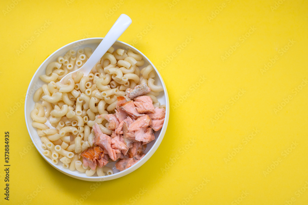 Sticker boiled pasta with boiled fish on child plate with spoon