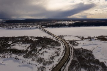 A view from a drone on a bridge over a river covered with ice and snow. Winter, cold day. The sun and the clouds.