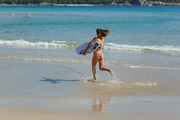 Fototapeta premium young beautiful girl in a swimsuit with a surfboard in her hands on the beach near the water, sea, summer, heat, sunny day, clear sea water, wave, lifestyle, sport, leisure, vacation, day off,