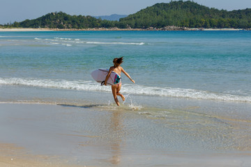 young beautiful girl in a swimsuit with a surfboard in her hands on the beach near the water, sea, summer, heat, sunny day, clear sea water, wave, lifestyle, sport, leisure, vacation, day off,